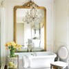 Enchanting Bathroom Design High Quality and Value to Your Home Décor: Elegant Ample Mirror With Carving Frame In Golden Tone Reflects The Pretty Chandelier Above The Sleek White Bathtub With A Classic Wooden Chair Near The Window